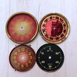 Peut inclure: Quatre cadrans de montre circulaires. Deux cadrans présentent des dégradés rouge et or avec le texte "Маяк" et des chiffres dorés. Un cadran a un centre rouge profond avec des chiffres dorés et un cadre doré. Un cadran noir porte le texte "ZENIT".