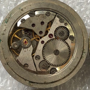 May include: Close-up view of a silver watch mechanism with visible gears and the number 2214 printed on the face.