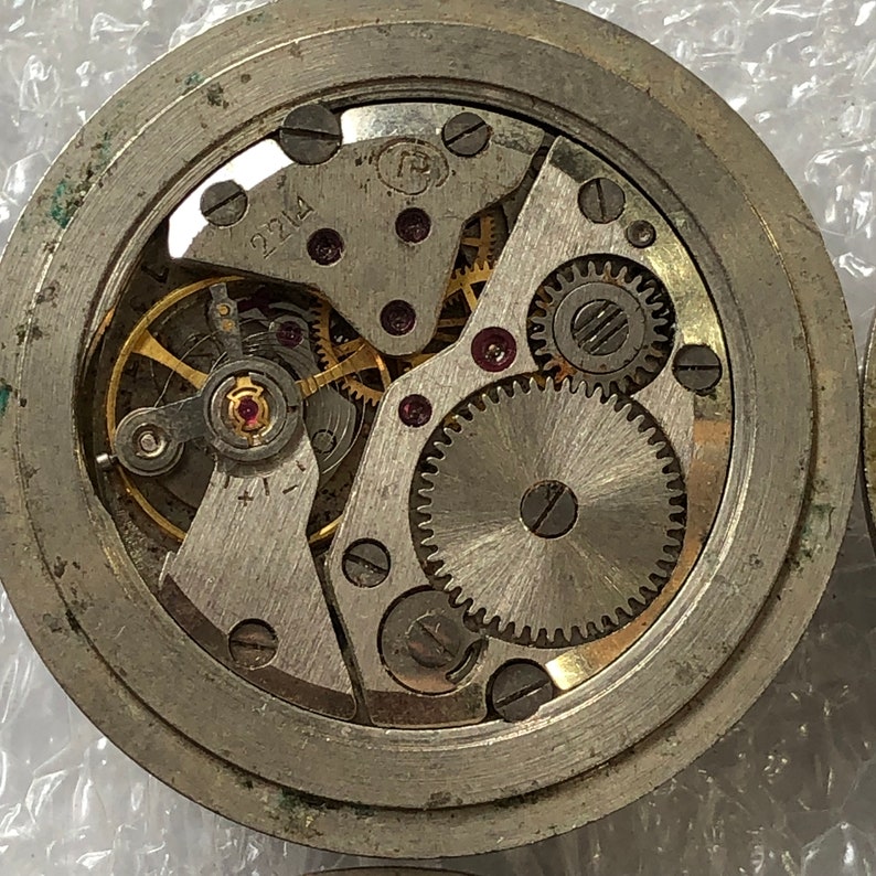 May include: Close-up view of a silver watch mechanism with visible gears and the number 2214 printed on the face.