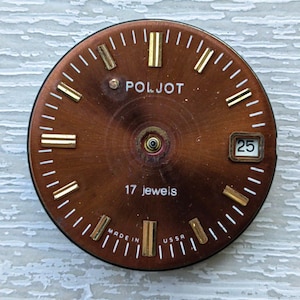 May include: A vintage watch face with a brown dial and gold-colored hour markers. The watch face has the brand name "POLJOT" and the text "17 jewels". The date window displays the number "25". The words "MADE IN USSR" are also visible.