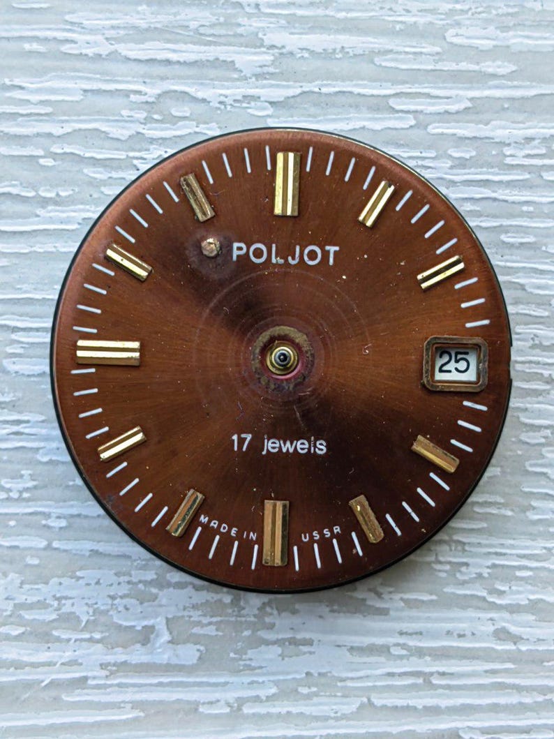 May include: A vintage watch face with a brown dial and gold-colored hour markers. The watch face has the brand name "POLJOT" and the text "17 jewels". The date window displays the number "25". The words "MADE IN USSR" are also visible.