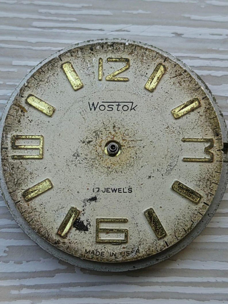 K&ouml;nnte beinhalten: Vintage Wostok Zifferblatt mit cremefarbenem Zifferblatt und goldfarbenen Stundenmarkierungen. Das Zifferblatt zeigt die Zahlen 12, 3, 6 und 9. Der Text "Wostok" und "17 JEWELS" sind sichtbar. Die Worte "MADE IN USSR" sind ebenfalls sichtbar.