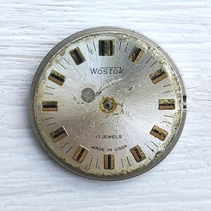 May include: A vintage silver watch face, branded "Wostok", with black text and gold and black rectangular hour markers. The text "17 Jewels Made in USSR" is also visible.