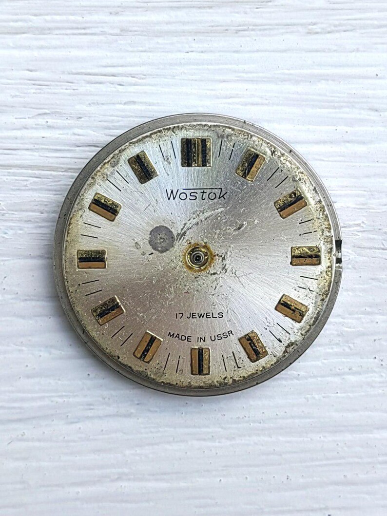 May include: A vintage silver watch face, branded "Wostok", with black text and gold and black rectangular hour markers. The text "17 Jewels Made in USSR" is also visible.
