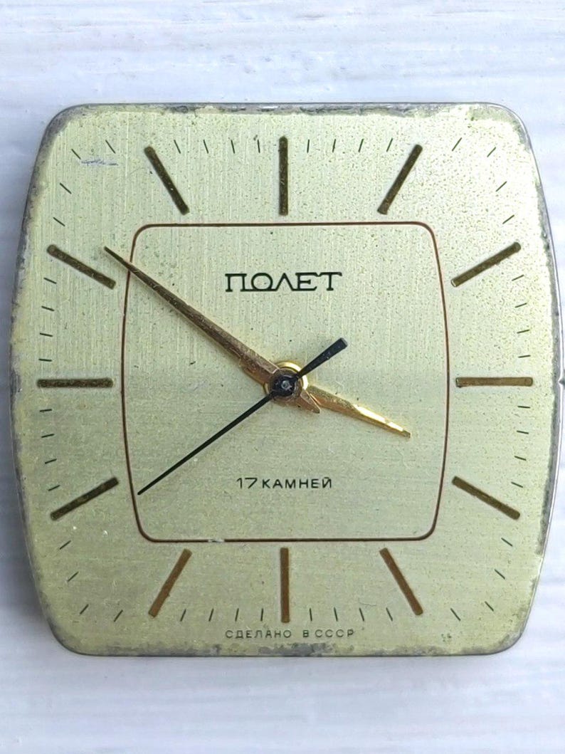 May include: A vintage gold-toned square clock with the word "ПОЛЕТ" in black. The clock face has black and gold hands and the text "17 KAMHEЙ" and "СДЕЛАНО В СССР". The clock has a brushed metal finish.