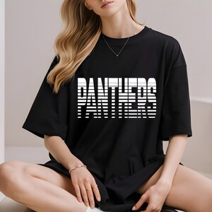 May include: Black t-shirt with the word "PANTHERS" in white, block letters. The word is made up of horizontal lines. The shirt has short sleeves and a relaxed fit.