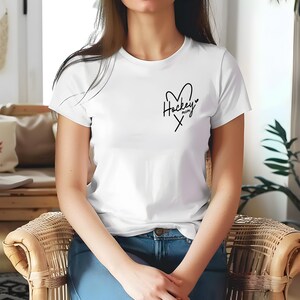 May include: White t-shirt with a black heart and the text "Hockey Mom" inside the heart.
