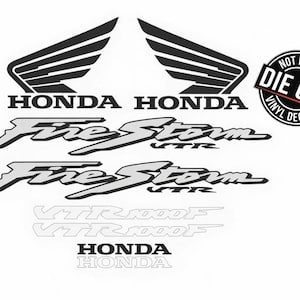 Op de afbeelding: Een set zwarte en zilveren vinylstickers met twee Honda-vleugellogo's, twee FireStorm VTR-tekstafbeeldingen, twee VTR1000F-omtrekken en twee Honda-woordmerken. Een ronde zwarte badge rechtsboven bevat de tekst NOT PRINTED DIE CUT VINYL DECAL.