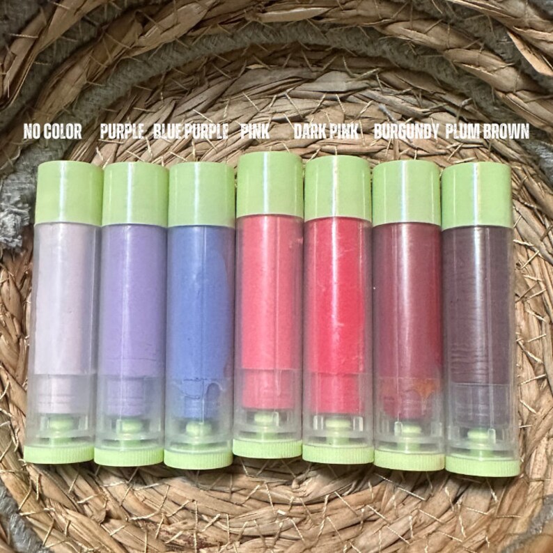 K&ouml;nnte beinhalten: Eine Sammlung von Lippenbalsam in transparenten Tuben mit hellgr&uuml;nen Kappen. Die Balsame sind in verschiedenen Farben erh&auml;ltlich, darunter Lila, Rosa und Burgunderrot. Der Text &uuml;ber den Balsamen lautet "NO COLOR, PURPLE, BLUE PURPLE, PINK, DARK PINK, BURGUNDY, PLUM BROWN."
