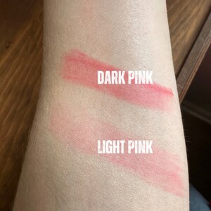K&ouml;nnte beinhalten: Nahaufnahme eines Arms mit zwei rosa Lippenstiftmustern. Das obere Muster ist mit "DARK PINK" und das untere mit "LIGHT PINK" beschriftet. Die Farbmuster sind auf der Haut aufgetragen und zeigen die Farbunterschiede.