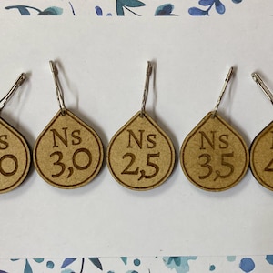 Könnte beinhalten: Fünf Holzetiketten mit Metallringen, jedes mit dem Text "Ns" gefolgt von einer Zahl und einem Komma. Die Zahlen sind 20, 30, 25, 35 und 40.