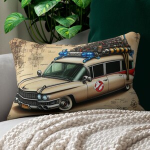 Può includere: Cuscino rettangolare beige con un'illustrazione vintage dell'Ecto-1 di Ghostbusters. Il design include uno sfondo in stile blueprint e il logo Ghostbusters. Il veicolo ha luci blu e attrezzature.
