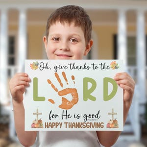 May include: A white sign held by a child with the text "Oh, give thanks to the LORD for He is good HAPPY THANKSGIVING." The word "LORD" is in large green letters with an orange handprint in the center. Pumpkins and crosses are also featured.