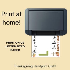 May include: A black printer printing a Thanksgiving handprint craft on letter-sized paper. The printed design includes text that says "Oh, give thanks" and "for He is HAPPY THANK". The design also features a cross, pumpkins, and leaves.