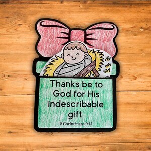 May include: A handmade Christmas card shaped like a gift box with a red bow. The card features a drawing of a baby in a manger, with the text "Thanks be to God for His indescribable gift" and the Bible verse 2 Corinthians 9:15.
