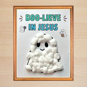 Puede incluir: Una impresión enmarcada con el texto "BOO-LIEVE IN JESUS" en letras azul verdoso y azul. La obra incluye dos pequeñas ilustraciones de fantasmas y una figura central de fantasma hecha con bolas de algodón blanco, ojos negros y una sonrisa.