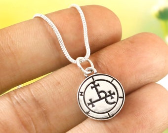 May include: Silver necklace with a pendant featuring a black and white sigil. The sigil is a circle with a cross in the center and a symbol that looks like a stylized letter 'L' with a cross on top.