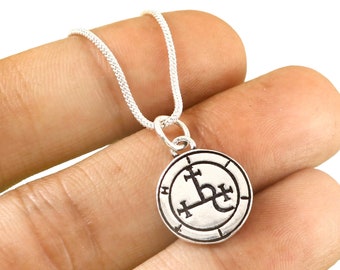 May include: Silver chain necklace with a silver pendant featuring a black sigil. The sigil is a circle with a cross in the center and a symbol that looks like a stylized 'L' with a cross on top.