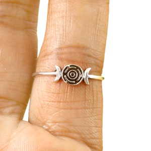 Pode incluir: Um anel de prata com uma lua tripla e um c&iacute;rculo com um design em espiral.