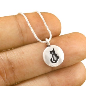 May include: A silver chain necklace with a round pendant featuring a black silhouette of a cat.