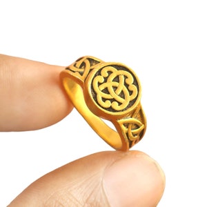 May include: A gold ring with a Celtic knot design. The knot is in a circular shape and is raised from the surface of the ring.