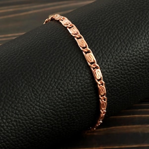 May include: A rose gold chain bracelet with a delicate, intricate design. The bracelet is made of a smooth, polished metal and has a secure clasp.