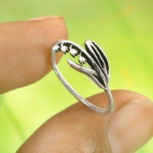Peut inclure: Une bague en argent avec un motif de muguet. La bague est ouverte et présente un motif floral délicat.