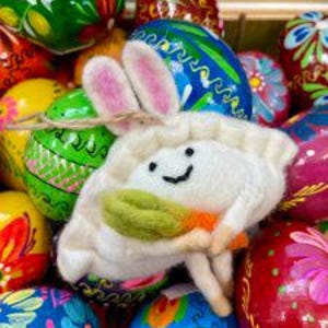 May include: A white felt bunny-eared dumpling ornament with a green leaf and orange carrot, surrounded by colorful painted Easter eggs.