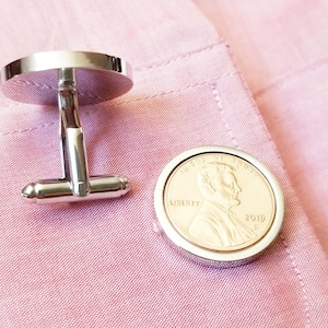 May include: Silver cufflinks with a round, coin-shaped design featuring a copper-colored image of Abraham Lincoln and the text "LIBERTY" and "1919".