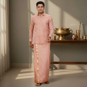 Puede incluir: Un atuendo tradicional indio rosa claro, que consta de una camisa de manga larga y una falda envolvente a juego. La falda presenta un borde dorado. El atuendo lo lleva una persona de pie en una habitación con una mesa de madera y objetos decorativos.