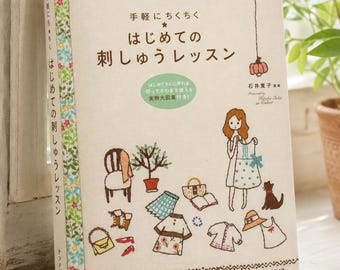 Puede incluir: Un libro de instrucciones de tapa blanda titulado "手軽にちくちく はじめての刺しゅうレッスン" con una cubierta de color crema que presenta ilustraciones estilo bordado de una persona, ropa, accesorios y un gato. El lomo tiene un patrón floral y el título.