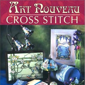 May include: A book cover with the title "Art Nouveau Cross Stitch" and the subtitle "Decorative Designs from the Turn of the Century". The cover features a variety of stained glass lamps, a pillow, and flowers.