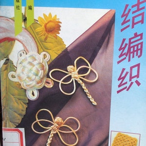 Op de afbeelding: Een boek met een blauwe kaft en de tekst "结绳编织" in rood. Het boek bevat afbeeldingen van een witte en gele schildpadknoop, twee gele libellenknopen en een gele vierkante knoop.