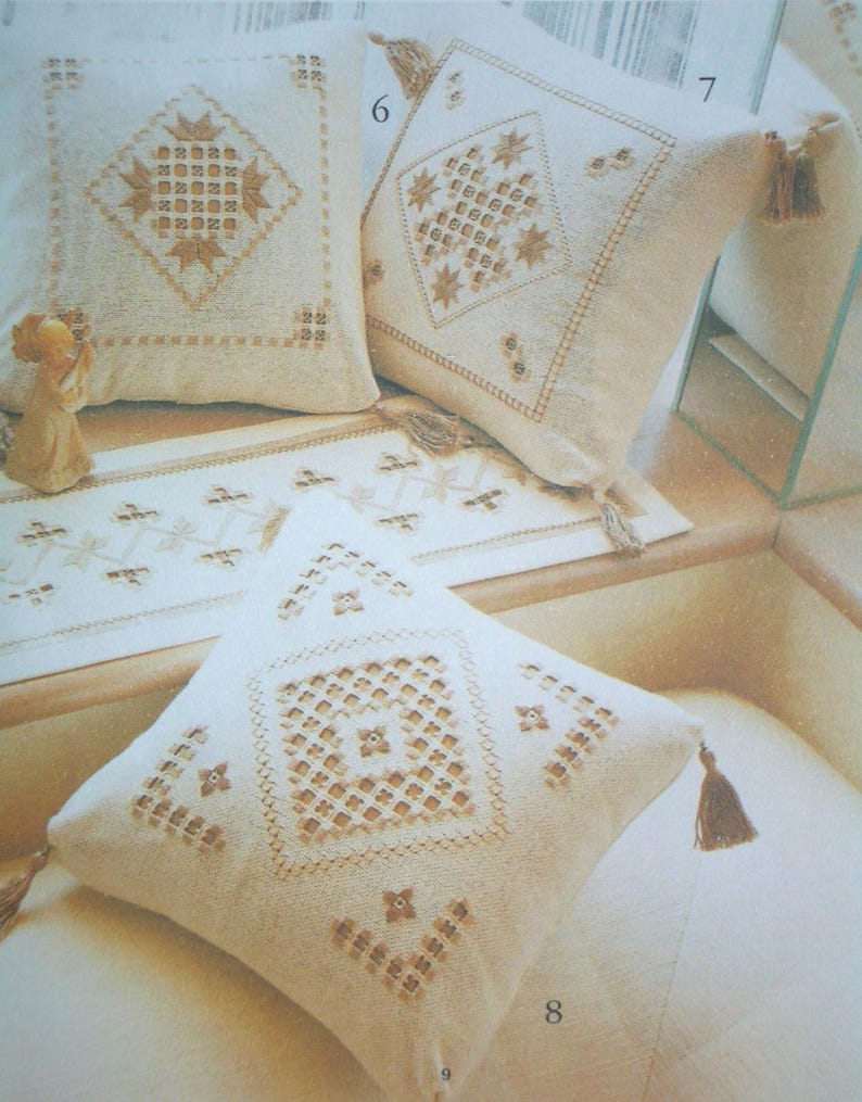 May include: Three square off-white throw pillows and a matching rectangular table runner, each featuring intricate tan embroidery in geometric diamond patterns. The pillows are finished with small corner tassels and labeled with the numbers 6, 7, 8, and 9.