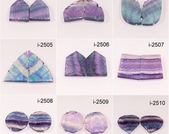 May include: Nine pairs of carved fluorite cabochons in various shapes and colors, including purple, blue, and white. The cabochons are arranged in three rows of three pairs.