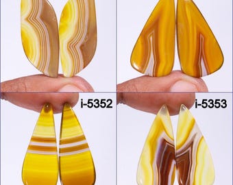 Pode incluir: Quatro pares de cabochões de ágata amarela, marrom e branca, cada par etiquetado com um identificador único: i-5350, i-5351, i-5352 e i-5353.