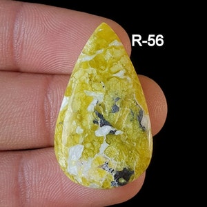 May include: A yellow, white, and black teardrop-shaped cabochon gemstone with a mottled pattern. R-56