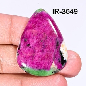 Könnte beinhalten: Ein polierter Edelstein in Tropfenform. Der Stein hat eine leuchtende magenta Farbe mit schwarzen und weißen Einschlüssen. Ein grünes Band verläuft entlang der Unterkante. Der Text "IR-3649" ist in Schwarz gedruckt.