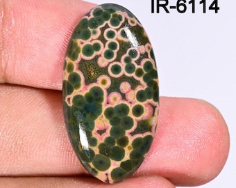 May include: An oval-shaped gemstone with a unique pattern of dark green and light pink circular spots. The stone has a polished surface and the text "IR-6114" is visible in the upper right corner. This gemstone could be used for jewelry making.