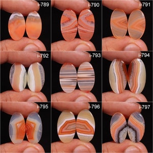 May include: Nine pairs of oval-shaped agate cabochons with various patterns of orange, white, and grey banding. The cabochons are arranged in three rows of three pairs.