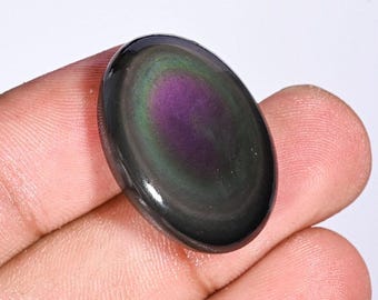 May include: An oval-shaped, polished obsidian gemstone with a swirling pattern of purple, green, and black. The stone is held in a hand, and the text "IR-7827" is visible in the upper right corner.