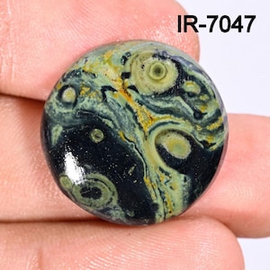 以下が含まれることがあります： 濃い緑色、黒色、黄色、明るい緑色の渦巻き模様が施された、丸く磨かれた宝石。 石は光沢のある仕上がりで、テキスト「IR-7047」が表示されています。 宝石は手で持たれています。