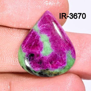 Puede incluir: Una piedra preciosa verde y rosa en forma de lágrima con un patrón de remolino. La piedra preciosa está tallada en cabujón y tiene una superficie lisa y pulida. IR-3670