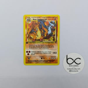 May include: A Mega Charizard X&Y Pokémon card with a yellow border. The card features a fiery orange and blue Charizard illustration. The card text includes "220 HP" and "Crimson Inferno". A white sticker with "BCD CARDS" is on the right.