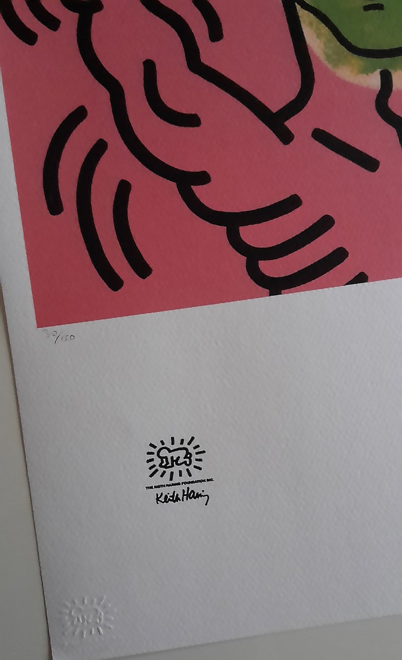 May include: A pink and green print with black outlines of a figure with a raised arm. The print is numbered 3/100 and signed "Keith Haring" with a sunburst logo.