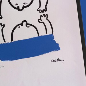 Puede incluir: Impresi&oacute;n art&iacute;stica abstracta con dos figuras estilizadas con contornos negros, bloques de color rojo y azul, y la firma del artista. La obra de arte est&aacute; sobre papel blanco y enmarcada en negro.