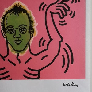 May include: A pink and green print of a man with a black outline. The man is wearing glasses and has a green face. The man is surrounded by black lines and a black and white creature with teeth. The print is signed "Keith Haring" in the bottom right corner.