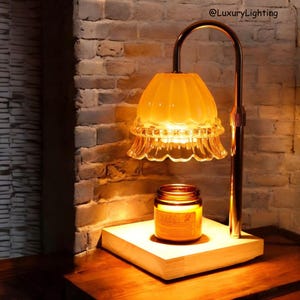 May include: A copper lamp with a scalloped glass shade illuminates a candle on a wooden base. The lamp is on a wooden table.