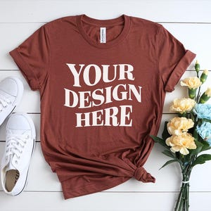 Könnte beinhalten: Ein rostfarbenes T-Shirt mit dem Text "YOUR DESIGN HERE" in weiß auf der Vorderseite.