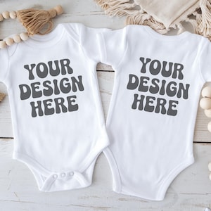 May include: Two white baby onesies with short sleeves. The onesies have the text "YOUR DESIGN HERE" printed in gray on the front and back.